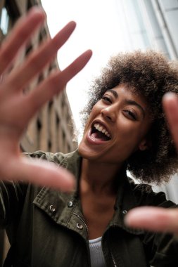 Neşeli kıvırcık kadın model ellerini kameranın önüne koyuyor. Gülümsüyor ve dar bir sokakta poz veriyor. Pozitif tutum konsepti.