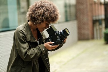 Dışarıda büyük bir analog kamera kullanan tutkulu ve çekici bir kadın. Gülümsüyor ve ekrana bakıyor. Sanat konseptini yapmak için eski moda yollar..