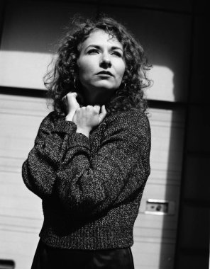 Dışarıya bakan genç modelin siyah beyaz portresi. Güneşli bir sabah ve arka planda bazı gölgeler var. Kazak giyiyor ve kolları vücudunun etrafında..