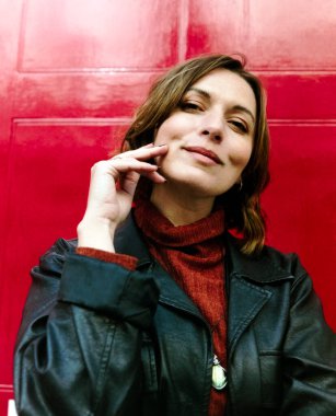 Kırmızı kapının önünde poz veren gülümseyen kadın portresi. Kafası eğik ve yüzüne dokunuyor. Orta formatlı bir kamera ile yapılmış renkli bir film görüntüsü..