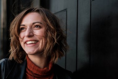 Gözünü kaçıran doğal bir kadının fantastik portresi. O, siyah bir kapıya yaslanıyor. Gülümsüyor ve başka tarafa bakıyor..