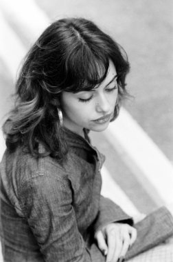 Sokakta oturan genç bir kadının yüksek monokrom portresi. Eski klasik bir kamerayla yapılan analog film görüntüsü. Düşünceli bir ifadeyle aşağıya bakıyor..