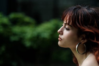 Yeşil arka planı olan sakin genç bir kadının yan portresi. Onun saçı kırmızı ve büyük bir küpe takıyor. Melankolik ifade.