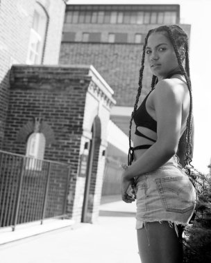 Dışarıdan kendine güvenen genç bir kadın kameraya bakıyor. O, sıcak yaz gününde rasta, şort ve bluz giyiyor. Tek renkli, analog bir film görüntüsü. Orta formatlı eski bir kamerayla yapılmış..