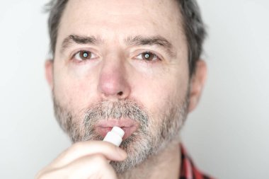 Orta yaşlı bir adamın dudak kremi sürerken, kuru ve nemlendirirken, dudakları çatlarken etkili dudak bakımı ve kış kuruluğuna karşı korunurken yakın plan portresi.