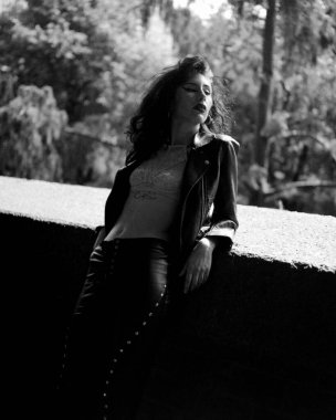 Dışarıdaki tırabzana yaslanmış kadın rock yıldızı. Siyah deri kıyafetler ve beyaz bir sütyen giyiyor. Bir film analog kamerasıyla yapılmış tahıllı bir resim.