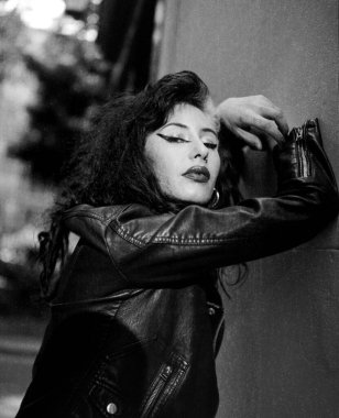 Duvara yaslanmış kadın müzisyen monokrom bir portrede kameraya bakıyor. Orta formatta yapılmış analog bir film görüntüsü. O bir rockçı siyah deri ceket giyiyor..