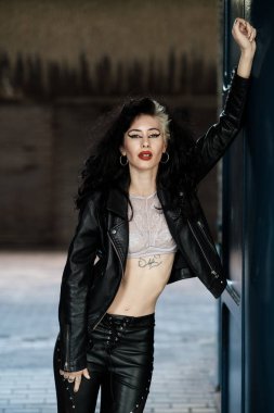 Mavi duvara dayanmış kadın rock yıldızının güzel bir portresi. Siyah deri ve beyaz bir bluz giyiyor ve ağır makyaj yapıyor..