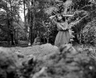 Grainy monokrom orta formatlı bir film. Genç bir kadının ormanda ellerini başının üstüne koyup poz verdiği bir fotoğraf.