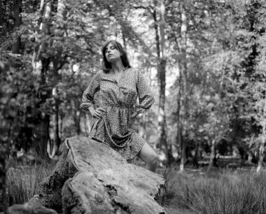 Ormanda poz veren genç bir kadının, görünür film tahılları ve yumuşak odak noktasıyla klasik bir estetik sergilediği siyah beyaz formatlı bir film.