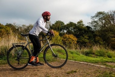 Bulutlu bir sonbahar gününde parktaki çakıllı yolda bisiklet süren bisiklet ve kask giyen bir erkek bisikletçi.