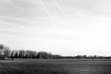 Grainy monochrome film photograph of contrails from airplanes filling the sky over middlesex filter beds nature reserve, a vast green space bordering the river lea or lee in london, england clipart