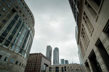 Kanarya iskelesindeki modern ofis binalarının düşük açılı görüntüsü, bulutlu bir gökyüzüne karşı çağdaş mimari sergileniyor, kentsel büyüme ve ekonomik faaliyeti vurguluyor