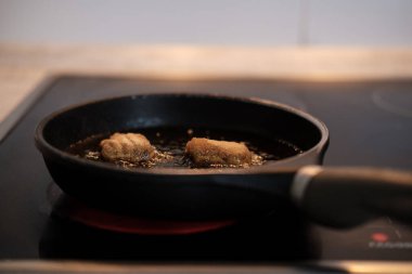 Modern bir cam tepside, siyah bir tavada sıcak yağda iki kızarmış tavuk kroketi pişirmek, çıtır çıtır, altın sarısı, kahverengi bir yemek yaratıyor ki bu hem lezzetli hem de her duruma uygun.