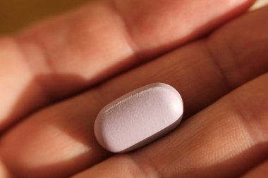 Tek bir pembe hapı açık elle tutarak, ilaç, sağlık, eczane kavramlarını, vitamin ve ilaçların tedavi ve sağlıktaki önemini,