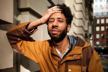 Düşünceli genç bir adamın portresi, elini alnına koymuş, kahverengi bir ceket giymiş, şehirde bir duvarın yanında duran, tefekkür ya da endişeyi ifade eden