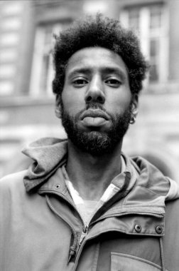 Afro saç stili ve sakallı, kapüşonlu ceket giyen, klasik, film benzeri estetik bir şey yapan genç bir adamın tek renkli tasviri.