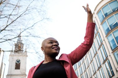 Pembe ceketli bir iş kadını, Londra 'da, arka planda St. Dunstan kilisesi olan bir taksiyi selamlıyor.