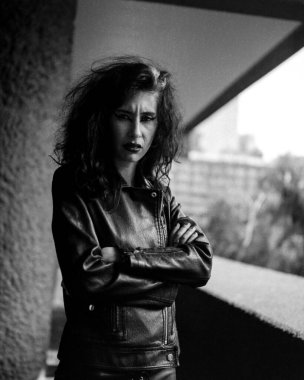 Dışarıdaki kızgın rock yıldızı görüntüsü. Dışarıda kaşlarını çatmış poz veriyor ve kameraya bakıyor. Bu tek renkli resimde siyah bir deri ceket giyiyor..