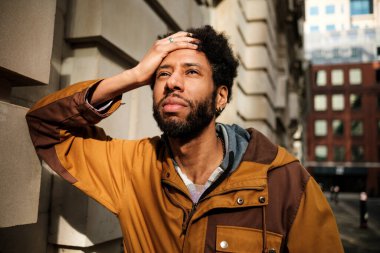 Genç Afro-Amerikalı bir adam, elini alnına koydu. Gündüz vakti şehir merkezinde dikilirken endişe ve endişe gösteriyor. Stres ve endişe duygularını dile getiriyor.