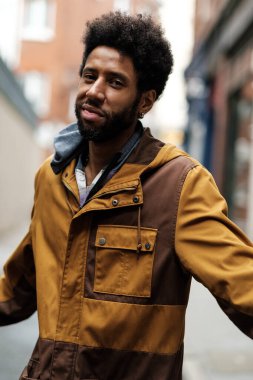 Kapüşonlu ceket giyen genç, şık bir zencinin portresi bulanık bir şehir sokağında dikilip kameraya bakarken modern moda ve havalı titreşimler yayıyor.