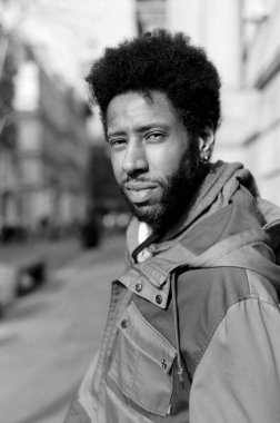 Kasvetli monokrom bir portre şık bir ceket giymiş genç bir adam yakalamak, hareketli bir şehir caddesinde güven içinde poz verirken doğrudan kameraya bakarak, kentsel cazibe yayıyor