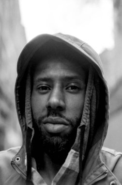 Taneli monokrom analog görüntü, sakallı, şık bir ceket giyen ve şehir ortamında poz veren, ciddi ve derin düşüncelere dalmış genç bir adamı yakalıyor.