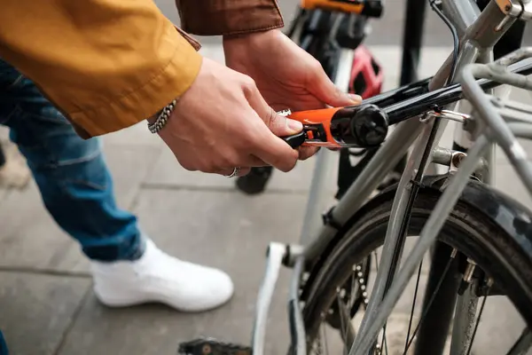 Bisikletçinin ellerinin U-Lock 'u kullanarak bir bisikleti rafa götürürken yakın plan görüntüsü, hayatla dolu bir şehir sokağında hırsızlığa karşı temel koruma sağlıyor.