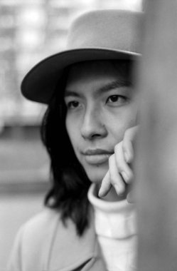 Şapka ve balıkçı yaka giyen düşünceli genç bir kadının tek renkli portresi, eli nazikçe çenesine dokunuyor, klasik, analog bir film estetiği yaratıyor.