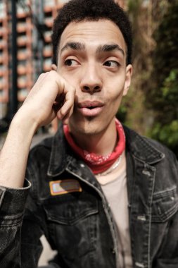 Kırmızı bandana takan şaşkın teslimatçı kameradan kafasını çevirirken çenesini tutuyor, ağzı açık bir şekilde şaşkınlık ve şaşkınlık içinde, gerçek bir merak anı yakalıyor.