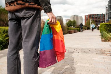 Bir şehir parkında yürürken elinde canlı bir gökkuşağı bayrağı tutan genç, gurur ayındaki şenlikler sırasında çeşitliliği, eşitliği ve lgbtq + haklarını neşeyle kutluyor.