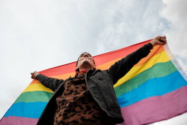 Genç adam gururla gökkuşağı bayrağı kaldırıyor, lgbtq + gururu, kapsayıcılığı ve toplumda eşit haklar ve kabulü simgeliyor.