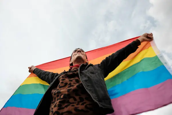 Genç adam gururla gökkuşağı bayrağı kaldırıyor, lgbtq + gururu, kapsayıcılığı ve toplumda eşit haklar ve kabulü simgeliyor.