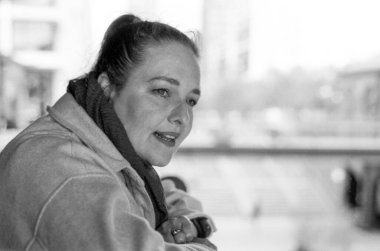 Grainy monochrome analog fotoğraf, 35 mm 'lik klasik bir kamera eşarp takan orta yaşlı bir kadını ve bulanık bir arkaplanı olan bir ceketi gösteriyor.