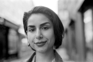 Gri monokrom analog fotoğraf, kısa siyah saçlı ve kısa küpeli gülümseyen bir genç kadın yakalamak, hafif bulanık kentsel bir arka plan üzerine kurulmuş