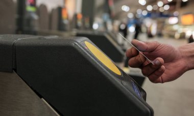 Bir okuyucunun yanında, metro ya da tren biletini ödemek için bağlantısız bir kredi kartı tutan bir el, toplu taşımaya hızlı ve kolay erişim olanağı sağlıyor.
