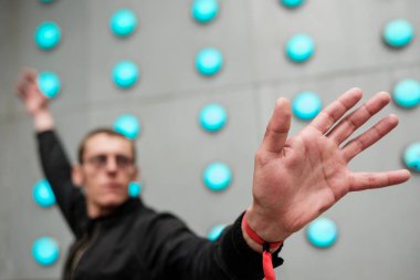 Kırmızı bileklik takan adam elinde dur işareti yapıyor. Arka planda mavi ışıklar olan etkileşimli bir duvar. Muhtemelen bir oyunu ya da sunumu kontrol ediyor.