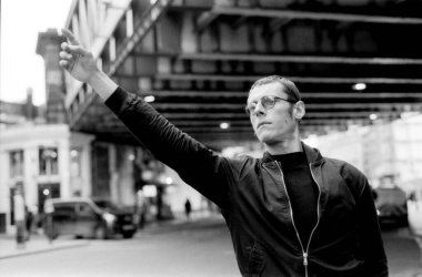 Tahıllı, siyah ve beyaz analog bir fotoğraf. Yükseltilmiş demiryolunun altındaki hareketli bir şehir sokağında taksiyi selamlayan genç bir adamı çekiyor. Eski ve samimi bir yaşam tarzını çağrıştırıyor.