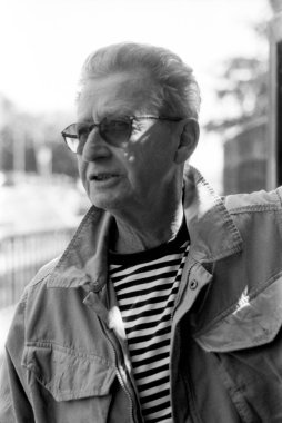 Yaşlı bir adamın güneş gözlüğü ve çizgili bir gömlek takıp klasik estetik ve dokulu bir hisle bir anı yakaladığı tek renkli, analog film portresi.