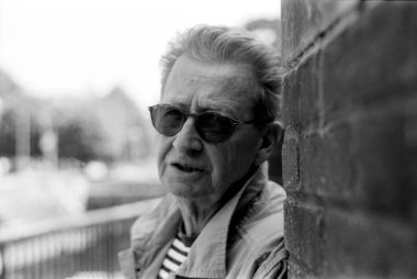 Yaşlı bir adamın güneş gözlüğü taktığı ve tuğla bir duvara yaslandığı, bulanık bir arka planı olduğu, klasik ve zamansız bir his yaydığı, tek renkli, tek renkli bir film portresi.