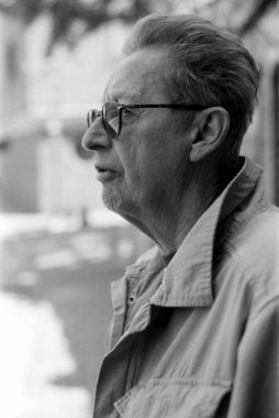 Grainy monokrom analog film portresi. Düşünceli, yaşlı bir adam gözlük takıyor. Muhtemelen 35 mm 'lik bir kamerayla çekiliyor.