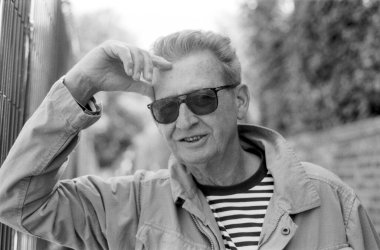 Taneli monokrom portresi güneş gözlüğü takan yaşlı bir adamın saçını düşünceli bir ifadeyle düzeltmesi nostalji ve ebedi bilgeliği çağrıştırıyor.