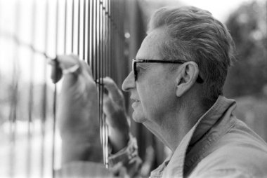 Grainy monokrom analog eski bir fotoğraf gözlüklü son sınıf bir adamın metal bir çitin arkasından dikkatlice gözlemlediğini eli nazikçe parmaklıklara dokunuyor.