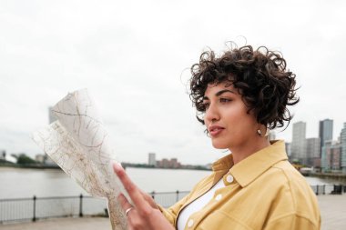 Nehir kenarındaki hareketli bir şehri gezerken elinde harita tutan genç bir turist, bir sonraki tatil yerini hevesle planlıyor ve yol boyunca yeni manzaralar keşfediyor.