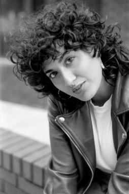 Tahıllı monokrom analog fotoğrafçılığı kıvırcık saçlı, deri ceketli ve büyük halka küpeli genç bir kadının klasik, kentsel bir estetik...