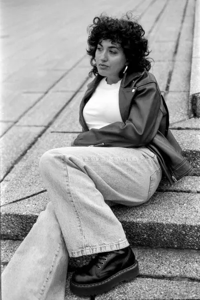 Deri ceket ve kot pantolon giyen genç bir kadının klasik bir 35 mm 'lik film kamerasıyla yakalanmış, zamansız bir şehir tarzı yayarken görüntüsü.