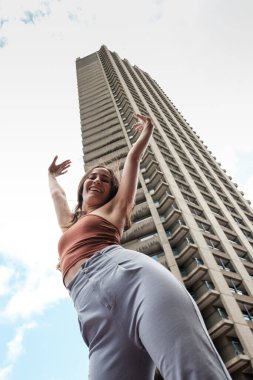 Londra 'daki barbika malikanesinin önünde özgürlüğünü ve neşesini ifade eden genç dansçı, kentsel gaddar mimarinin dinamik enerjisini vurguluyor.