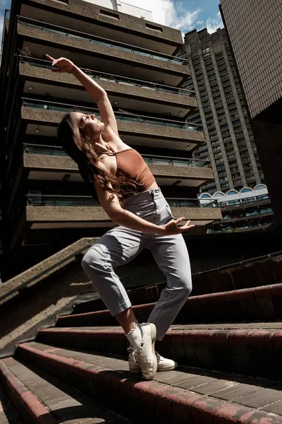 Barbican malikanesinin merdivenlerinde modern bir dans gösterisi sergileyen zarif bir dansçı. Londra 'daki barbar mimarinin çarpıcı bir örneği.