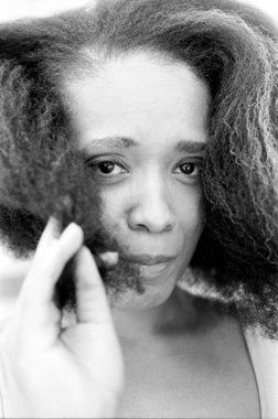 Uzun, kıvırcık saçlarıyla oynayan genç bir kadının tek renkli portresi. Uzağa dikkatlice bakarken yüzüne nazikçe dokunuyor. Güzellik ve duygu saçıyor.