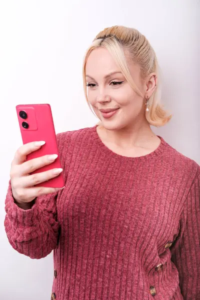 Sosyal medya içeriğini yaratmak için akıllı telefon kullanan, selfie çeken ya da video blogu kaydeden, pembe süveter giyen, beyaz arka planda